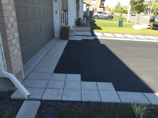 Beautifully landscaped front yard with interlock pavers, a garden bed with white stone accents, and a welcoming entryway.