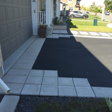 Beautifully landscaped front yard with interlock pavers, a garden bed with white stone accents, and a welcoming entryway.