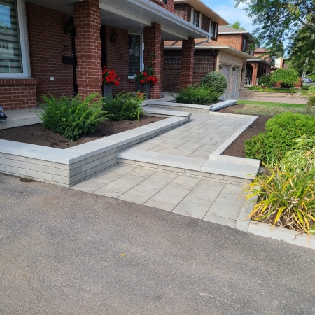 Beautifully landscaped front yard with interlock pavers, a garden bed with white stone accents, and a welcoming entryway.