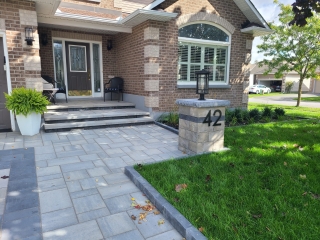 Elegant front entrance with modern interlock pavers, custom stone steps, and a stylish address pillar with lighting.