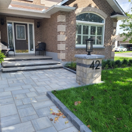 Elegant front entrance with modern interlock pavers, custom stone steps, and a stylish address pillar with lighting.
