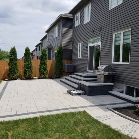 Modern backyard patio with interlock pavers, built-in steps, and seating area for outdoor living