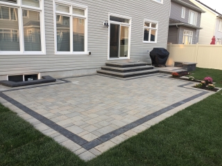 Modern backyard interlock patio with contrasting border design and multi-tiered stone steps.