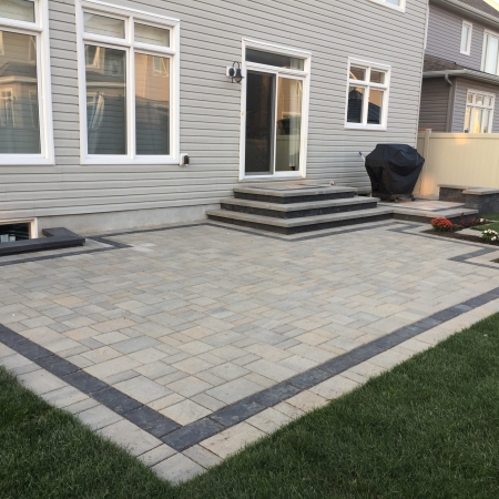 Modern backyard interlock patio with contrasting border design and multi-tiered stone steps.