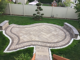 Modern backyard interlock patio with contrasting border design and multi-tiered stone steps.