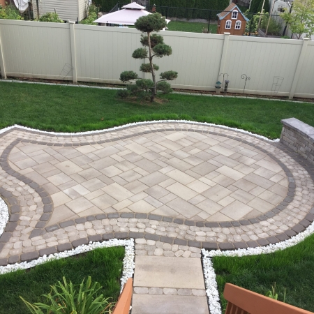 Modern backyard interlock patio with contrasting border design and multi-tiered stone steps.