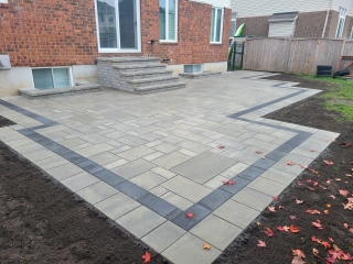 Modern backyard interlock patio with contrasting border design and multi-tiered stone steps.