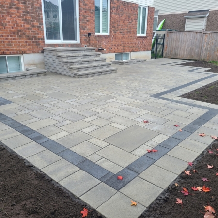 Modern backyard interlock patio with contrasting border design and multi-tiered stone steps.