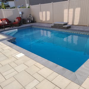 Spacious backyard pool deck featuring elegant stone pavers and a sleek border design.